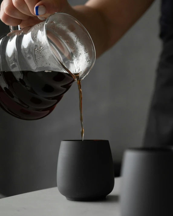 a person pours coffee into a cup, a still life, by Robbie Trevino, matte black, detail, glassware, coast