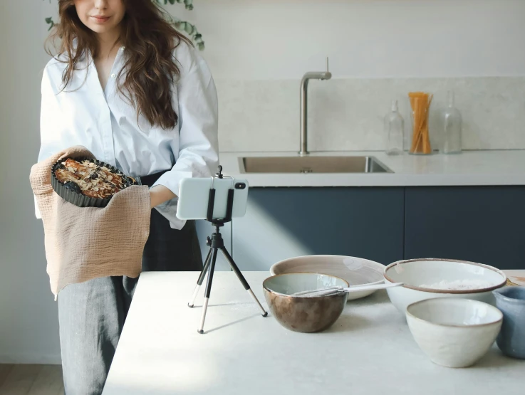 a woman standing in a kitchen holding a bag of food, a still life, unsplash, video art, tripod, japanese pottery, smartphone footage, high resolution photograph