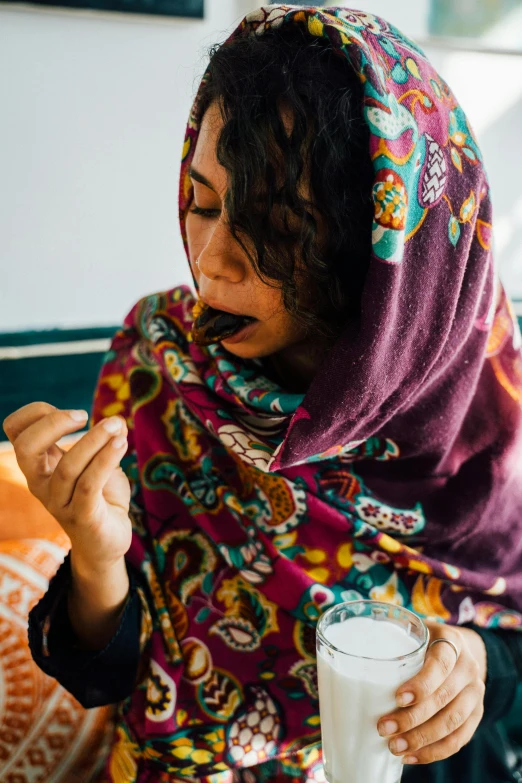 a woman sitting at a table with a glass of milk, by Riza Abbasi, pexels contest winner, hurufiyya, eating mars bar candy, someone in home sits in bed, 2 5 6 x 2 5 6 pixels, bangladesh