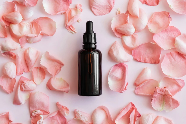 a bottle of essential oil surrounded by rose petals, by Elaine Hamilton, trending on pexels, pink gradient background, black roses in hair, manuka, thumbnail