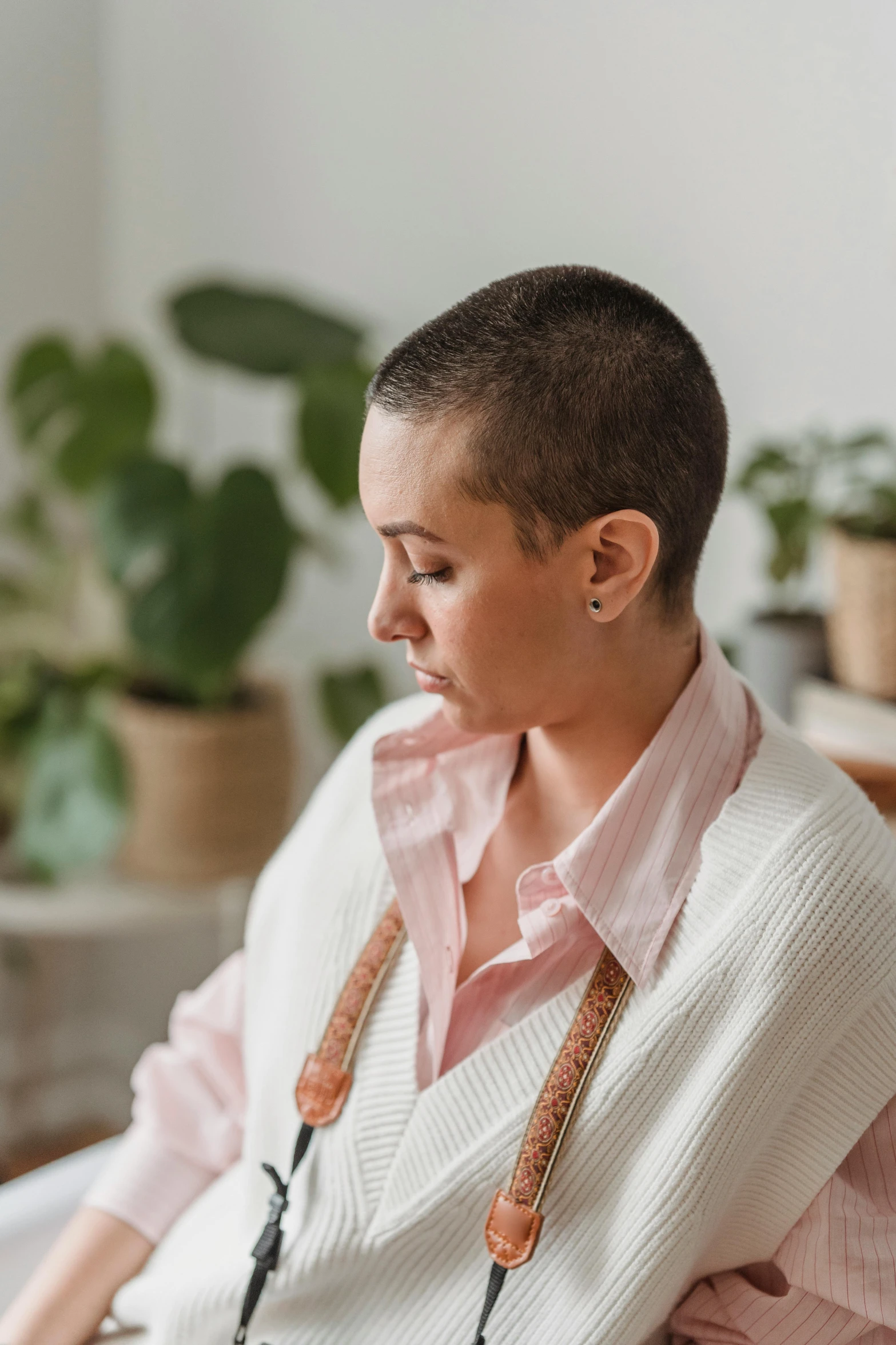 a woman sitting on a couch next to a potted plant, a portrait, by Jessie Alexandra Dick, trending on pexels, brown buzzcut, wearing a cardigan, on a white table, thoughtful )