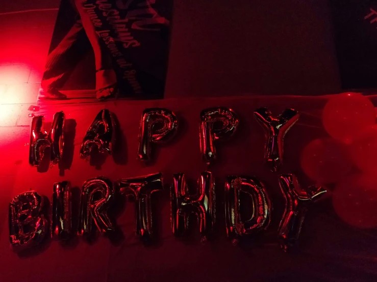 a person standing in front of a sign that says happy birthday, a picture, detailed red lighting, party balloons, dark and moody, not cropped