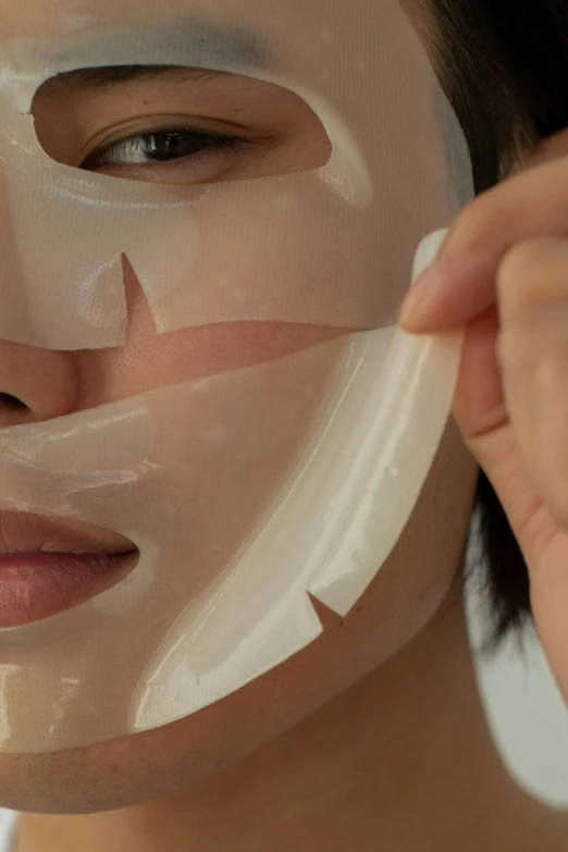 a woman is putting a mask on her face, inspired by Yu Zhiding, ultradetail face, wearing translucent sheet, small chin, medium - shot