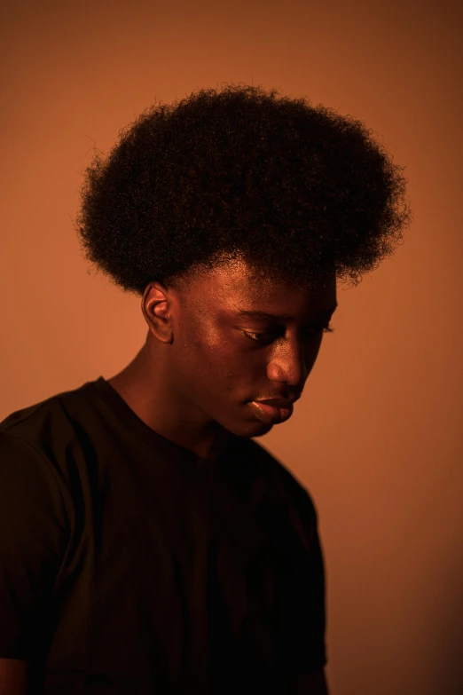 a man with an afro standing in front of a wall, trending on pexels, chiaroscuro soft lighting, portrait of depressed teen, ( brown skin ), androgynous male