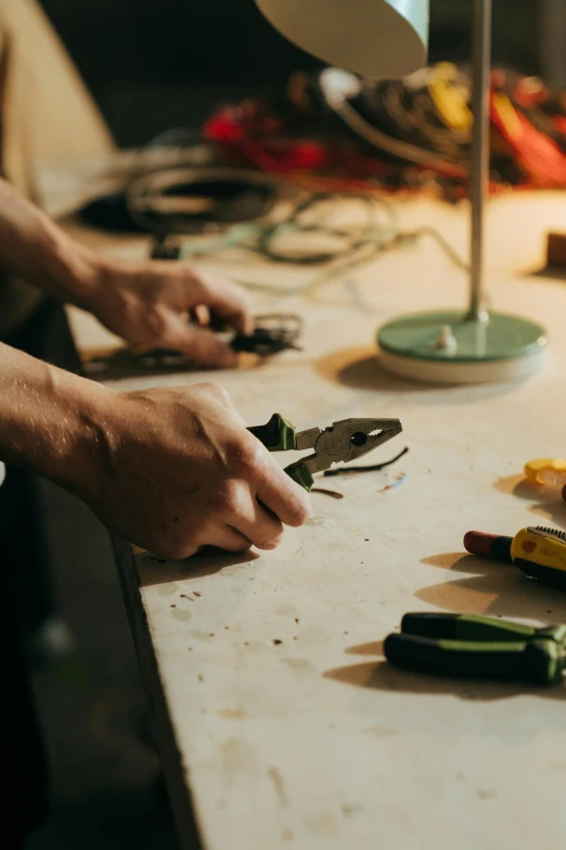 a person using a pair of pliers on a table, trending on pexels, in a workshop, exposed wires, objects well lit, sustainable materials