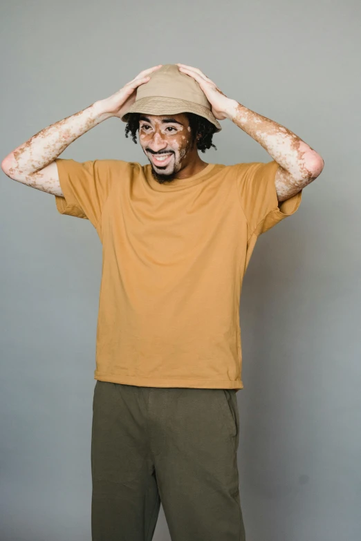 a man standing with his hands on his head, featured on reddit, baggy clothing and hat, ochre, wearing a t-shirt, muted brown