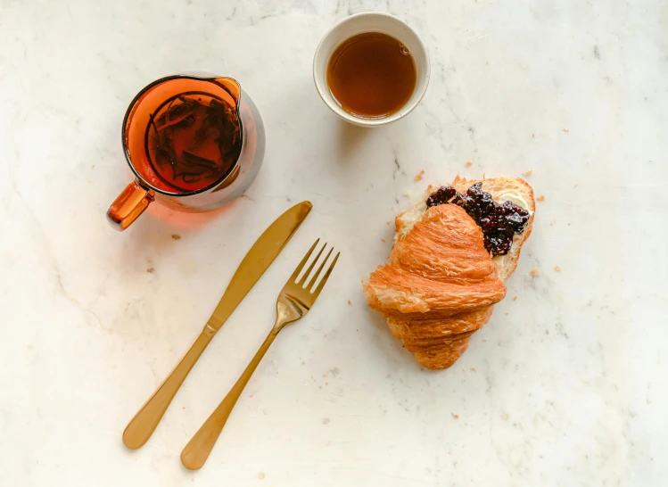 a table topped with a croissant and a cup of tea, inspired by Richmond Barthé, pexels contest winner, cutlery, black and terracotta, 15081959 21121991 01012000 4k, full body in shot