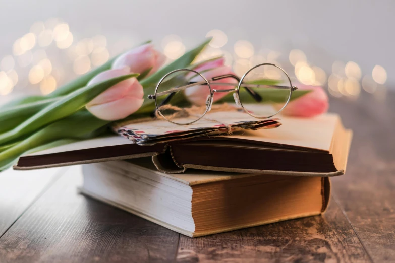 a stack of books with glasses and a bouquet of tulips, by Sylvia Wishart, trending on pixabay, romanticism, square rimmed glasses, lights with bloom, cottagecore hippie, uncropped