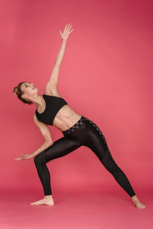 a woman doing a yoga pose against a pink background, arabesque, black spandex, hands on hips, fit pic