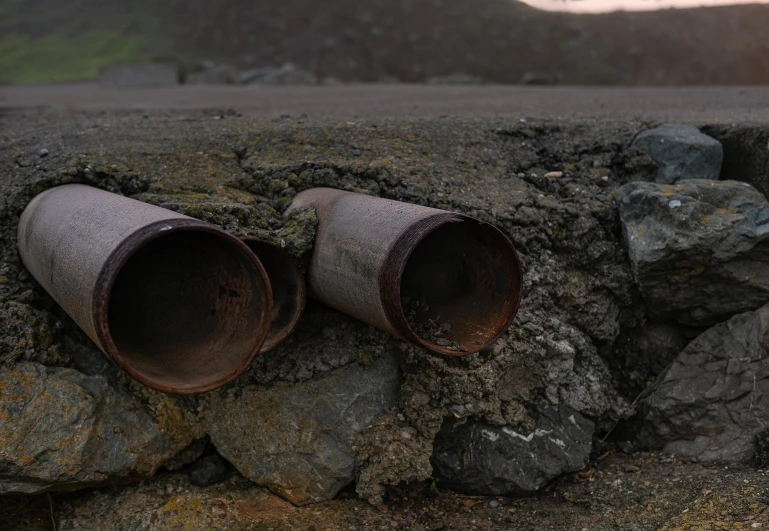 a couple of pipes sitting on top of a pile of rocks, an album cover, unsplash, land art, ((rust)), black sand, sewer, background image