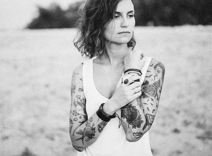 a black and white photo of a woman holding a cup of coffee, a black and white photo, by Lucia Peka, tribal tattoos right arm sleeve, anna nikonova aka newmilky, floral tattoos, near the beach