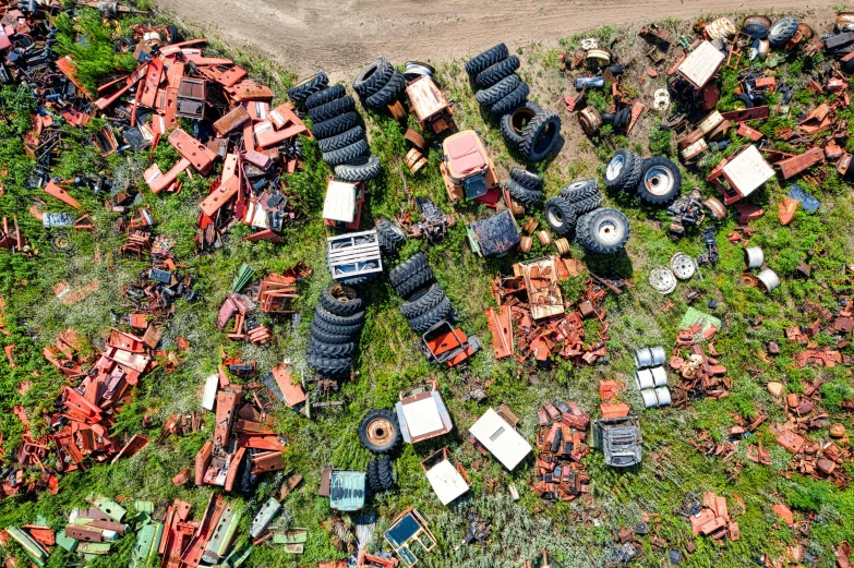 a pile of tires sitting on top of a lush green field, by Arnie Swekel, assemblage, drone photograpghy, rusty vehicles, crates and parts on the ground, a screenshot of a rusty