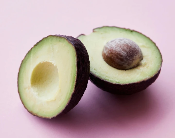 two halves of an avocado on a pink surface, trending on pexels, epicurious, brown, jen atkin, round-cropped