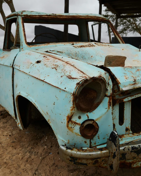 an old car that is sitting in the dirt, unsplash, photorealism, pale blue, square, cracked varnish, low quality photo