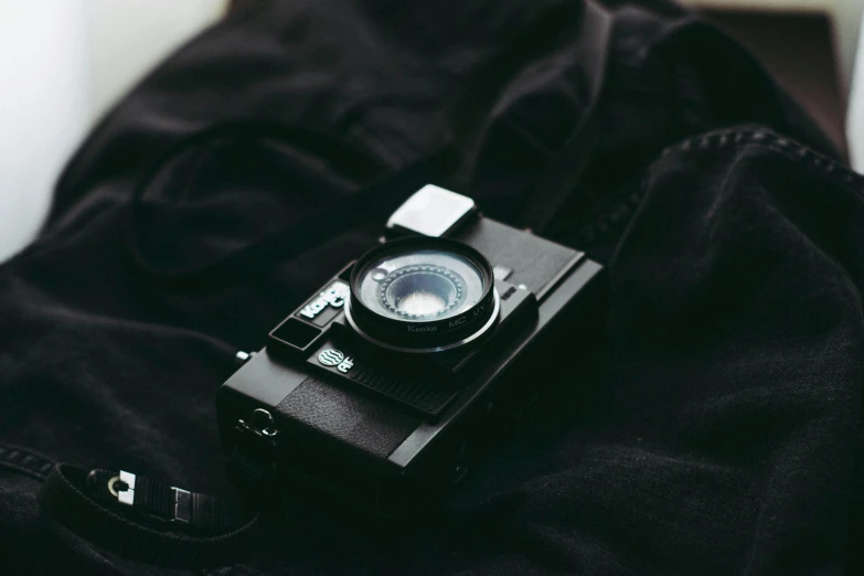 a black camera sitting on top of a black bag, unsplash contest winner, wearing black clothes, vintage film grain, cute photograph, medium format