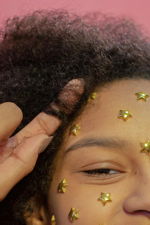 a young girl with gold stars on her face, trending on pexels, afrofuturism, scratching head, low quality photo, glitter sticker, top down shot