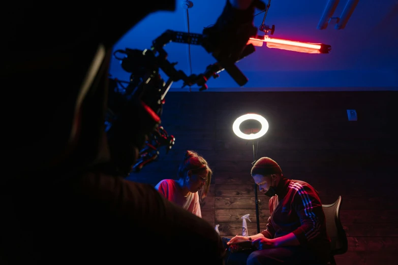 a man and a woman sitting in front of a camera, by David Begbie, pexels contest winner, red and blue back light, production still, ring lighting, on set