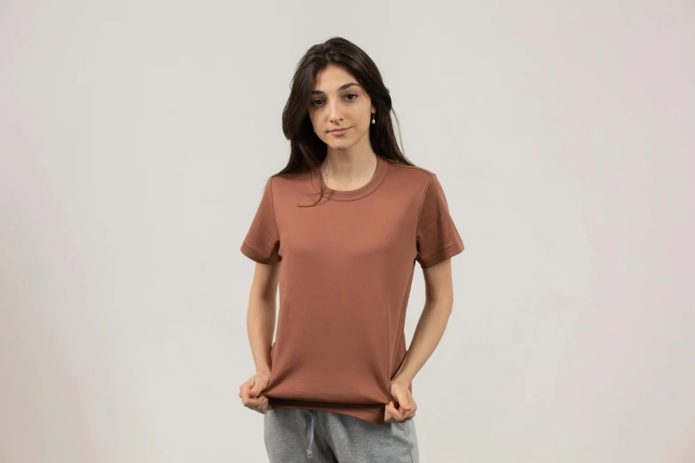 a woman standing with her hands in her pockets, a cartoon, unsplash, brown shirt, sport t-shirt, brown resin, premium