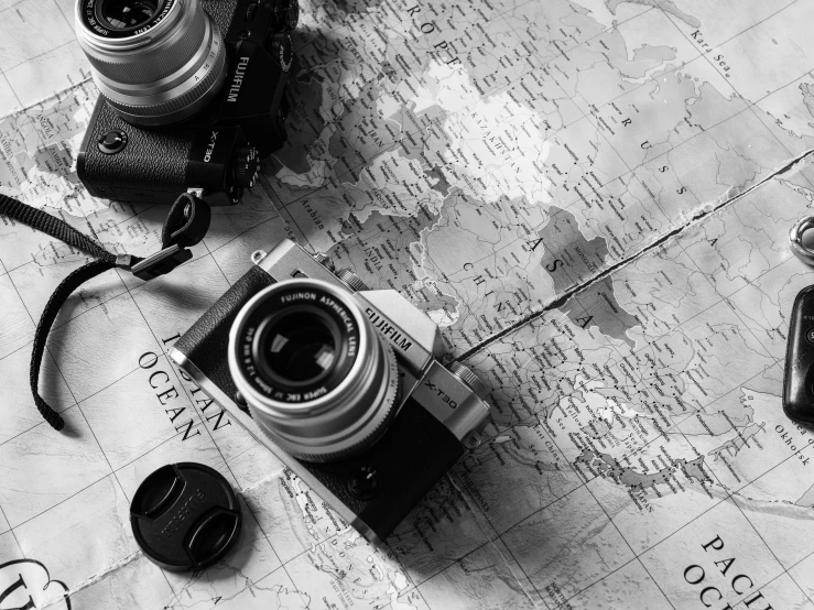 a couple of cameras sitting on top of a map, a black and white photo, fujifilm x - pro 2, cinematic. by leng jun, vacation, detailed medium format photo