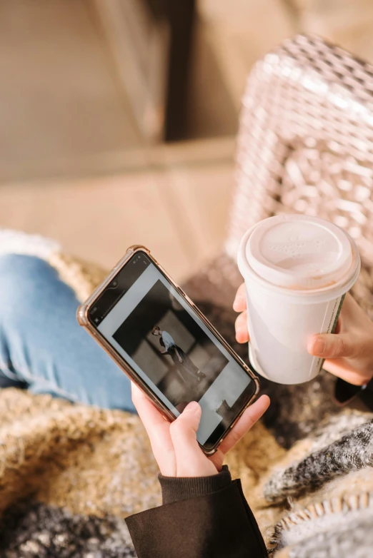 a woman sitting on a couch holding a cup of coffee, a picture, trending on pexels, happening, android cameraphone, digital oth, iced latte, 33mm photo