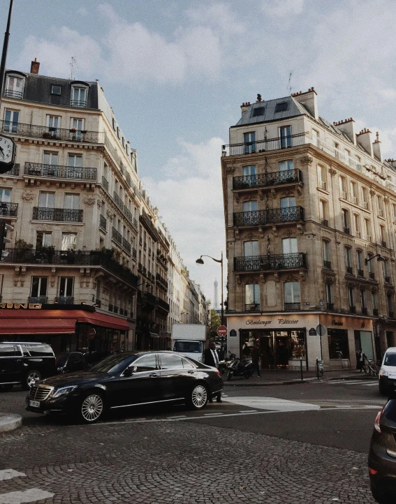 a group of cars driving down a street next to tall buildings, pexels contest winner, paris school, french village exterior, 🚿🗝📝, non-binary, buildings covered with greebles