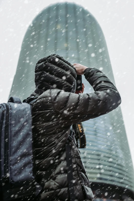 a person standing in front of a tall building in the snow, pexels contest winner, a backpack, paparazzi shot, covered head, cold texture