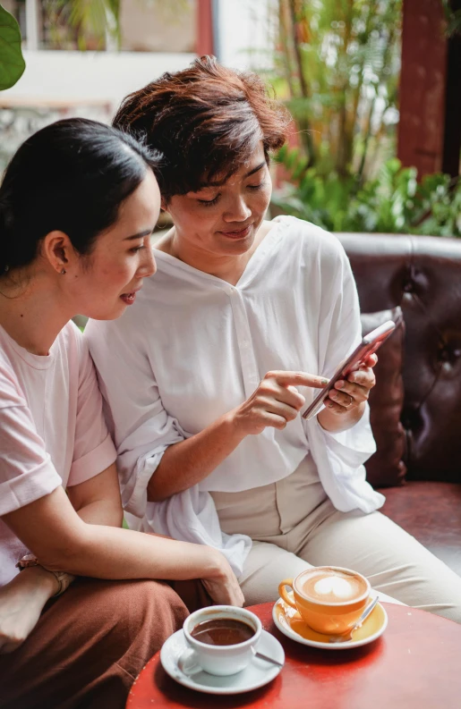 two women sitting on a couch looking at a cell phone, trending on pexels, indonesia, square, asian human, high-quality photo