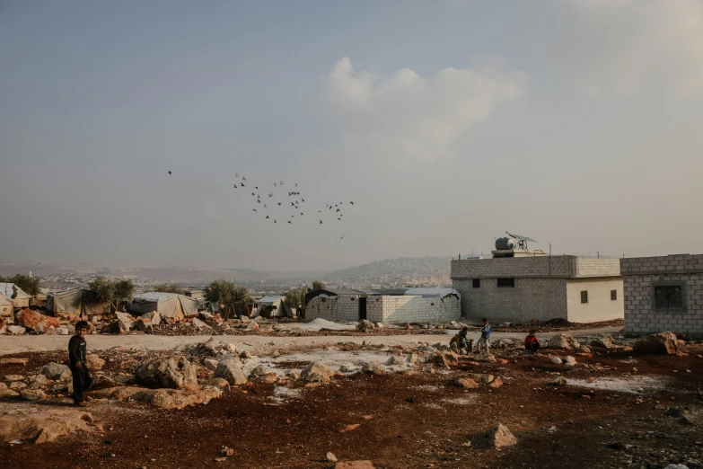 a group of people standing on top of a dirt field, les nabis, broken buildings, birds flying in the distance, aida muluneh, slide show