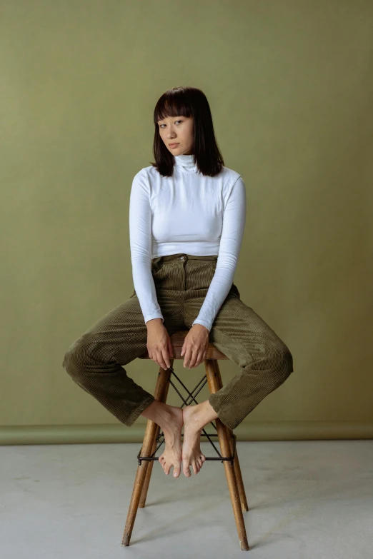 a woman sitting on top of a wooden chair, inspired by Kim Tschang Yeul, green corduroy pants, in white turtleneck shirt, rex orange county, wearing pants