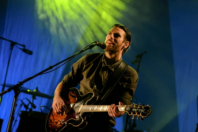 a man playing a guitar in front of a microphone, an album cover, pexels, figuration libre, bright eyes, concert, profile image, ben nicholas