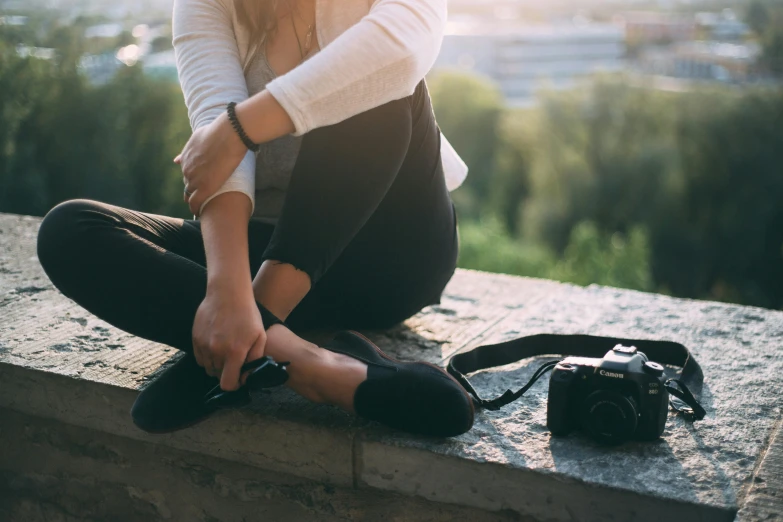 a woman sitting on a ledge with a camera, trending on pexels, her foot sticking out, scratches on photo, laces, black