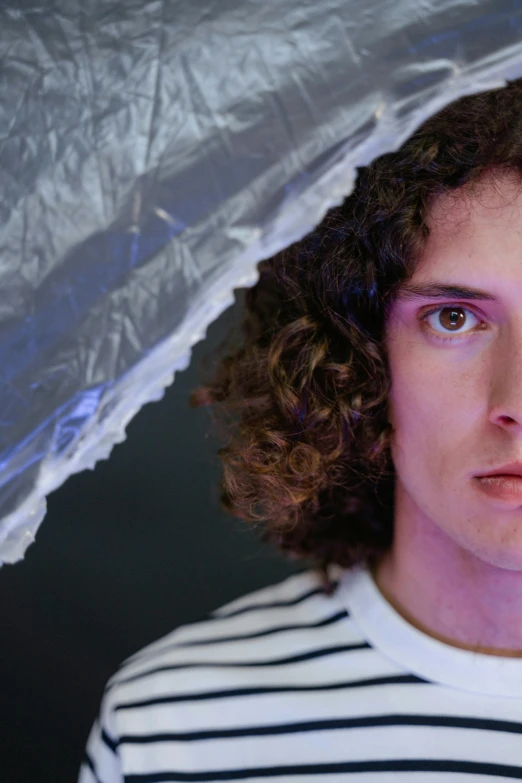 a young man holding an umbrella over his head, an album cover, inspired by Juan Carlos Stekelman, unsplash, with haunted eyes and curly hair, portrait of an android, close - up studio photo, concerned