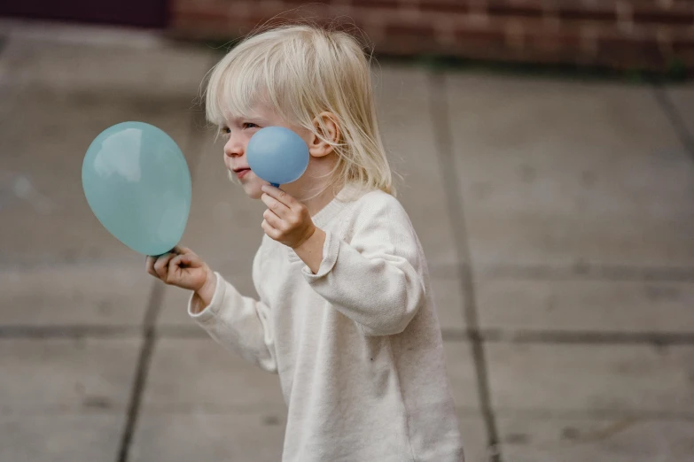 a little girl holding a blue balloon in one hand and a blue balloon in the other, an album cover, by Nina Hamnett, pexels contest winner, a plaster on her cheek, nordic pastel colors, children playing with pogs, street life