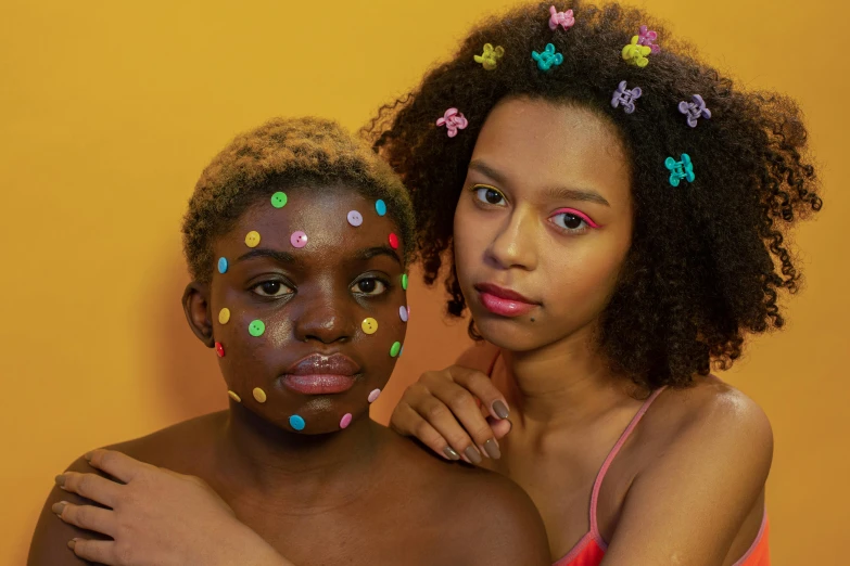 a couple of women standing next to each other, by Lily Delissa Joseph, trending on pexels, toyism, colored dots, yellow makeup, black teenage girl, bare forehead