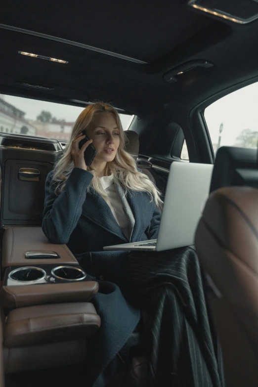 a woman sitting in the back seat of a car talking on a cell phone, trending on unsplash, renaissance, woman in black business suit, carriage full of computers, ( ( theatrical ) ), blonde