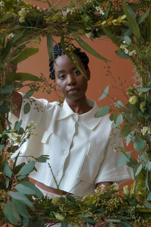 a woman standing in front of a mirror surrounded by greenery, inspired by Carrie Mae Weems, renaissance, wearing a white button up shirt, ikebana white flowers, lupita nyong'o, branches and foliage