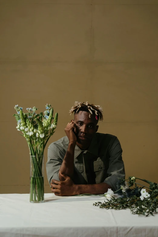 a man sitting at a table with a vase of flowers, an album cover, pexels contest winner, ( ( dark skin ) ), portrait pose, joel fletcher, riyahd cassiem