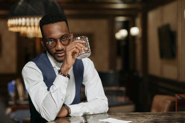 a man sitting at a table with a glass of water, inspired by William Grant Stevenson, pexels contest winner, renaissance, ( ( dark skin ) ), square rimmed glasses, bartending, attractive girl