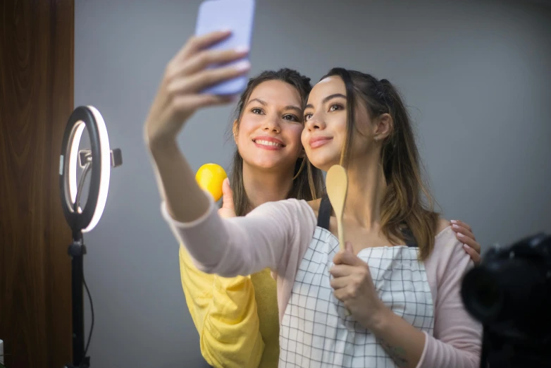 two women taking a selfie in front of a mirror, shutterstock, ring light, avatar image, food stylist, fluorescent