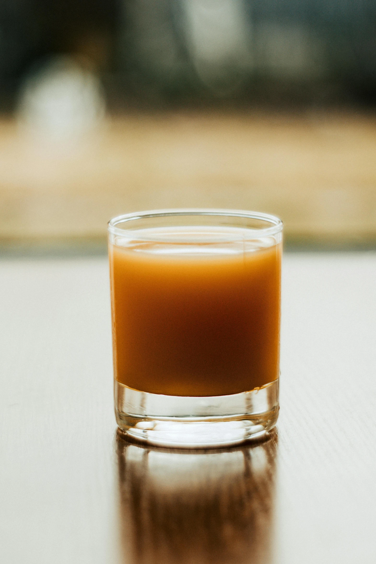 a glass of orange juice sitting on a table, by Jessie Algie, unsplash, caramel. rugged, from the elbow, gunpowder smoke, smooth color