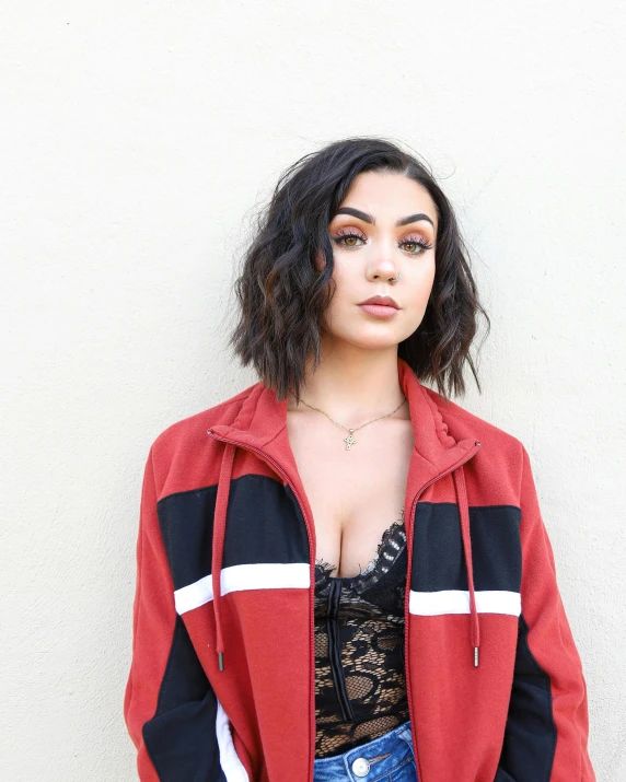 a woman standing in front of a white wall, an album cover, trending on unsplash, antipodeans, wearing red jacket, charli xcx, curly middle part haircut, kaitlyn michelle siragusa