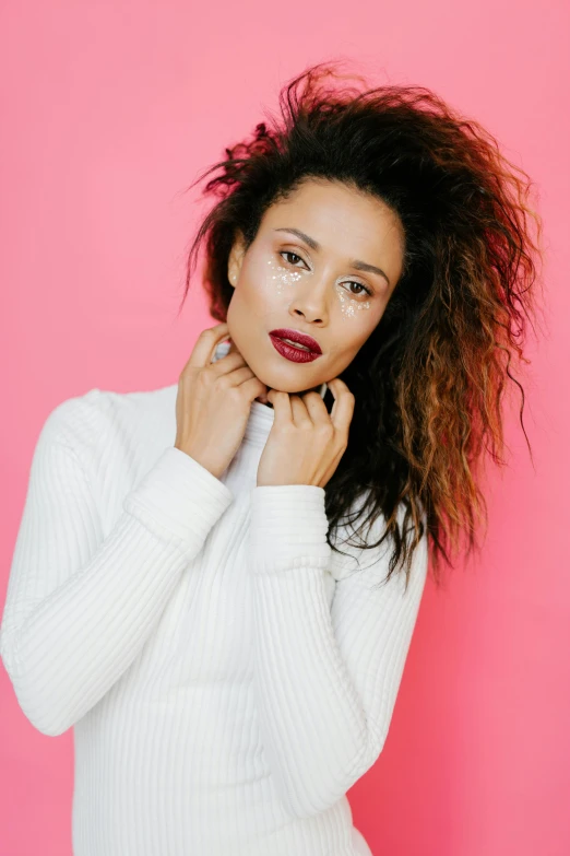 a woman in a white sweater posing for a picture, frizzy hair, lipstick, mixed race, in front of white back drop