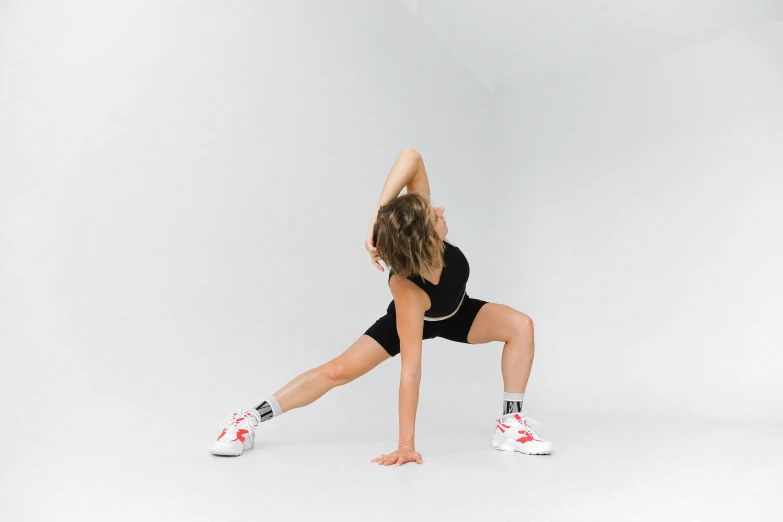 a woman doing a yoga pose on a white background, by Emma Andijewska, unsplash, arabesque, muscular thighs, sneakers, wearing leotard, body with black and red lava