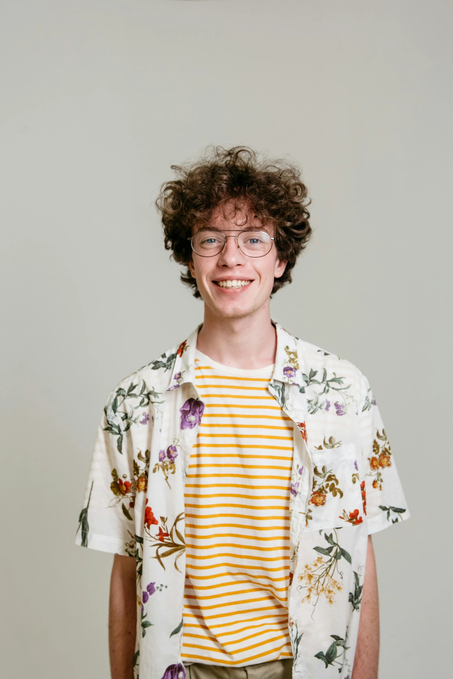 a young man standing in front of a white wall, by Jacob van Utrecht, trending on pexels, renaissance, he has short curly brown hair, with hawaiian shirt, rebecca sugar, twitch streamer