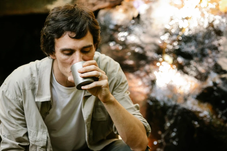 a man sitting on a rock drinking from a cup, lachlan bailey, profile image, forest picnic, avatar image