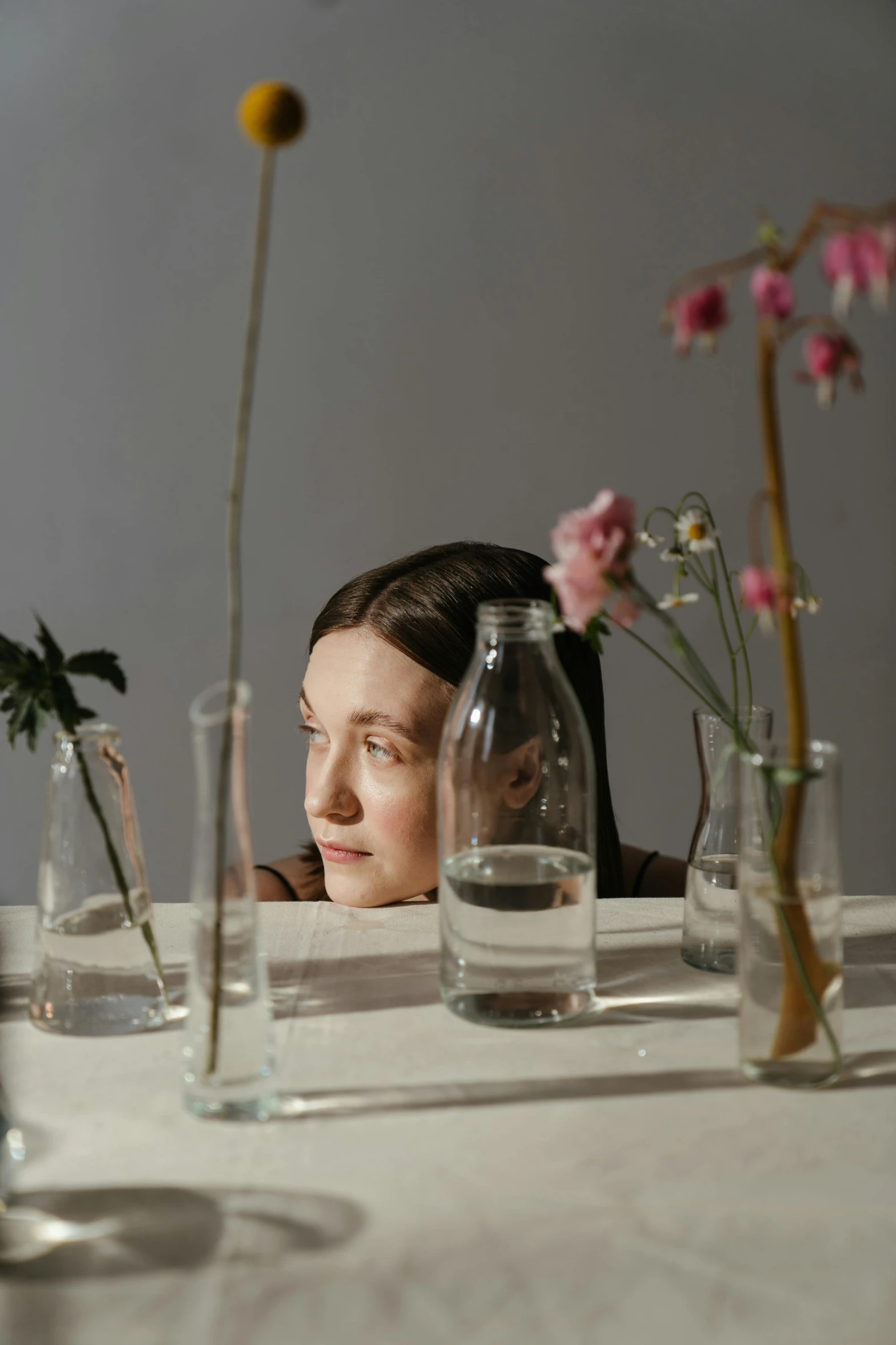 a woman sitting at a table with flowers in vases, inspired by Anna Füssli, looking to the side off camera, zoomed in, ignant, high quality photo