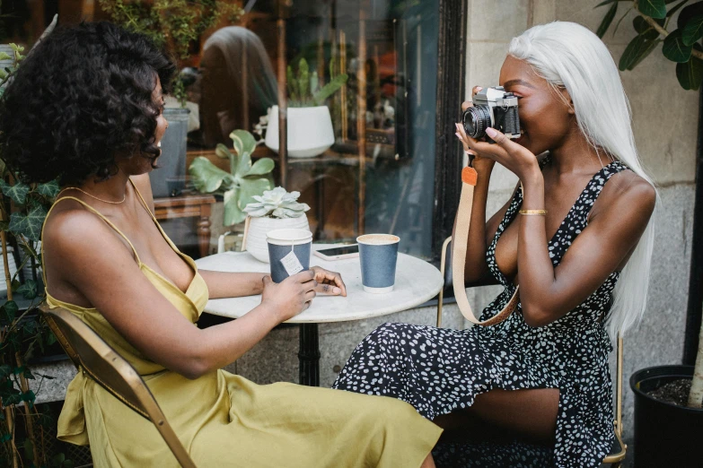 two women sitting at a table with a camera, trending on pexels, beautiful city black woman only, sitting on a mocha-colored table, medium format, cute photograph