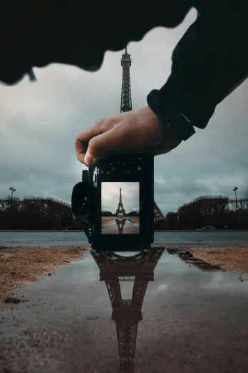 a person taking a picture of the eiffel tower, inspired by Jean Tabaud, unsplash contest winner, realism, reflection puddles, centered in a frame, holding nikon camera, image split in half