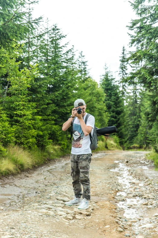 a man standing on a dirt road talking on a cell phone, a picture, inspired by Zoran Mušič, pexels contest winner, doing a sassy pose, forestry, holding a big camera, avatar image