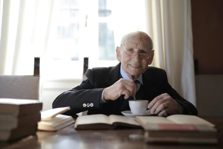 a man sitting at a table with a cup of coffee, a portrait, by Jan Tengnagel, unsplash, wilbur smith, rudolf weisse, an elderly, ap